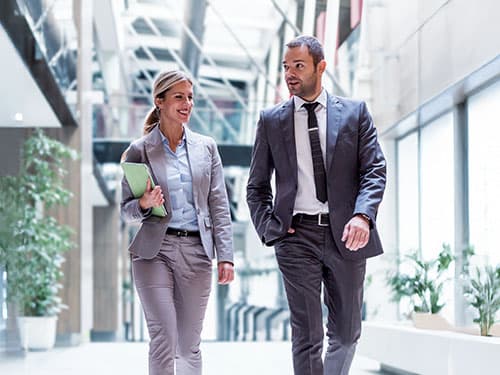 Two business professionals in conversation walking down modern building hallway. Two business professionals in conversation walking down modern building hallway.